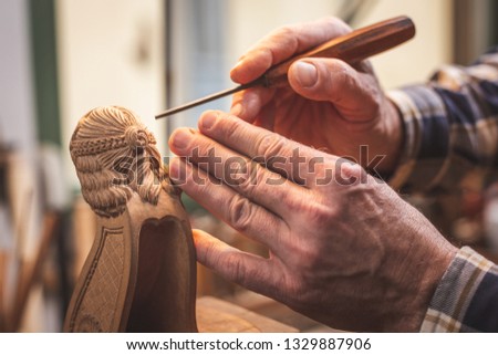 Hands of a wood sculptor working on a small wooden figure
