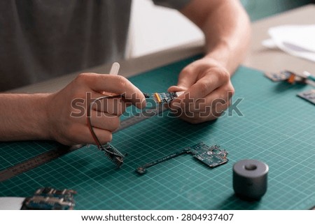 Hands work on a pcb connector with wires on a worktable filled with tools and circuit boards during the day