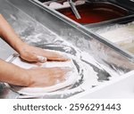 Hands work skillfully to flatten dough on a floured surface in a kitchen preparing delicious pizzas. Toppings and sauce await in nearby containers for assembly.