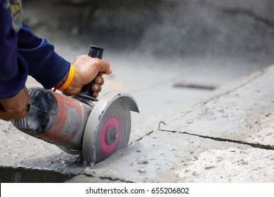 Hands of worker catching and using electric cutting machine tool to cut concrete floor with dirty dust spreading in air, copy space on the right.