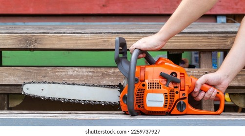 Hands of a worker with a chainsaw on a wood background. Concept worker lumberjack. Adjustment and maintenance of chainsaws. - Powered by Shutterstock