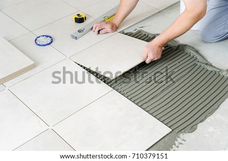 The hands of the worker are laying  the ceramic tile on the floor.