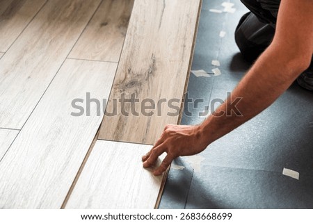 Hands of a worker positioning light laminate panels on insulating underlayment during apartment renovation, careful assembly of modern floating floor.