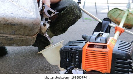 hands of a worker pouring gasoline into a lawn mower tank from an iron canister through a plastic funnel close-up, refueling a manual grass trimmer with fuel - Powered by Shutterstock