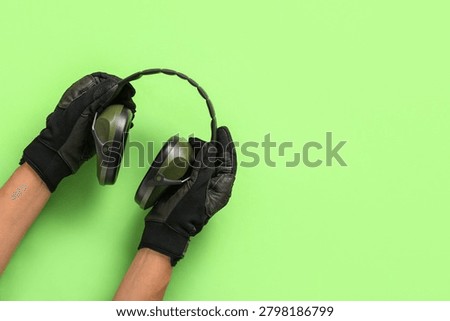 Hands of worker with protective earmuffs on green background