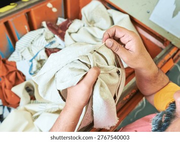Hands of a Worker sorting mixed fabric offcuts and textile waste from industrial bin for recycling and reuse. Industrial recycling programme aimed to cut costs and be better for the environment. 