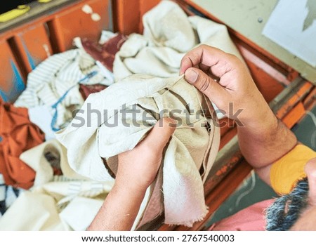 Hands of a Worker sorting mixed fabric offcuts and textile waste from industrial bin for recycling and reuse. Industrial recycling programme aimed to cut costs and be better for the environment. 