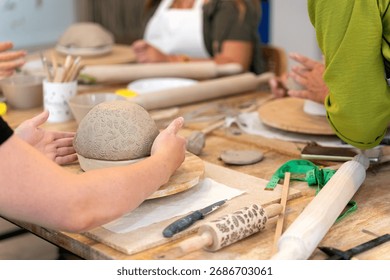 Hands working with clay, creating a patterned pot in a pottery class, focusing on creativity and craft