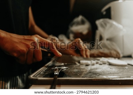 Hands working with dough on a baking tray in a kitchen setting with blurred background
