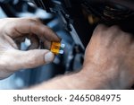 Hands working on a car, specifically handling an orange automotive fuse. Protecting the cars electrical circuits. Auto repair or electrical safety. Electrical car fuse or breaker. Automotive fuses