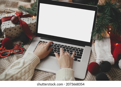 Hands working on laptop with blank screen on cozy bed with stylish christmas ornaments, present and santa hat. Christmas shopping online and freelance in holidays. Space for text - Powered by Shutterstock