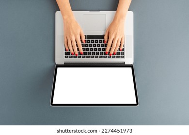 Woman’s hands working on laptop with empty screen on gray background. Office desktop with copyspace. Top view