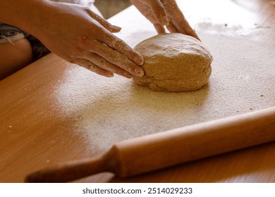 Hands working with a rolling pin on dough covered in flour. The image captures the traditional baking process on a wooden kitchen surface, highlighting a rustic home cooking experience - Powered by Shutterstock