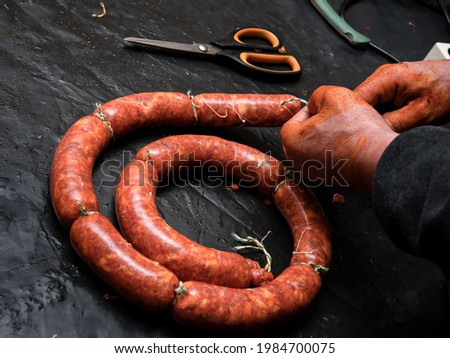 Hands of a working woman stained with adobo closing the intestines of the pig already stuffed with meat and spices and closing with rope to make sausages and let them smoke on a black table