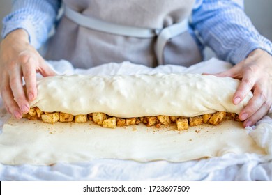 Hands wrap the dough with apple filling make apple strudel.Girl is preparing a pie at home in an apron.Work with puff pastry.The process of making apple strudel.Mom makes a pie.Apple strudel roll.