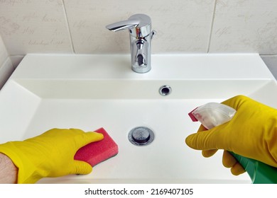 Hands in yellow protective gloves hold a sponge and cleaning agent for cleaning sanitary equipment in the bathroom. Chores and washbasin cleaning