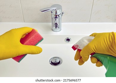 Hands in yellow protective gloves hold a sponge and cleaning agent for cleaning sanitary equipment in the bathroom. Chores and washbasin cleaning