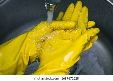 Hands In Yellow Rubber Gloves Close-up. A Man Washes Disposable Gloves Under The Tap With Water. Concept Of Home Cleaning Or Work Of A Medical Worker.