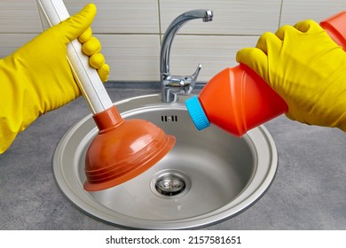 Hands in yellow rubber gloves hold a plunger and a pipe cleaner against the background of a kitchen sink. Housework cleaning a clogged sewer drain