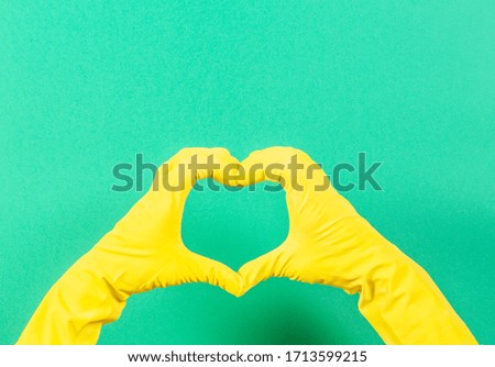 Hands in yellow rubber gloves making heart shape with fingers, on green background