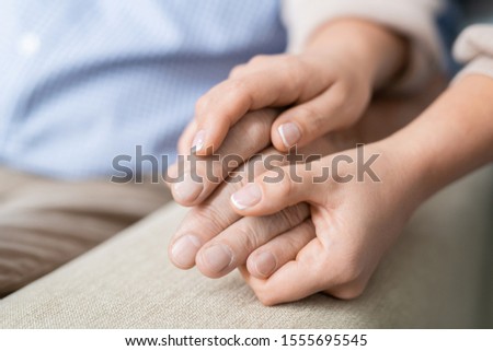 Hands of young affectionate and careful daughter holding that of her senior father expressing love and togetherness