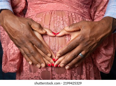 Hands Of Young African American Black Couple Forming A Heart Shape On The Pregnant Belly Of The Woman With Man's Hands On Top Showing Love Of Mom And Dad For Unborn Baby