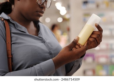 Hands of young African American woman in blue shirt holding yellow plastic bottle with spray deodorant or some other cosmetic product