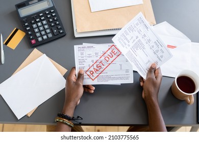 Hands of young African male holding unpaid bill over other papers and invoices while sitting by table - Shutterstock ID 2103775565
