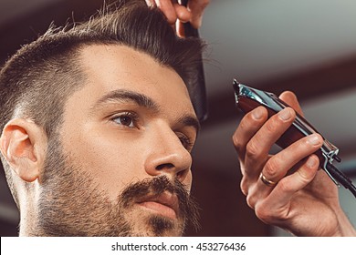 The hands of young barber making haircut to attractive man in barbershop