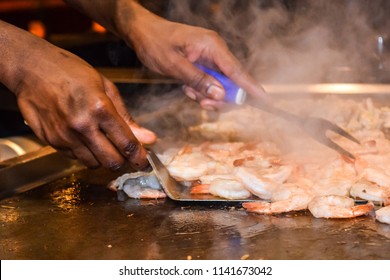 Hands Of A Young Black Male Chef Holding Utensils Preparing Shrimp At Table Side Service In Restaurant 