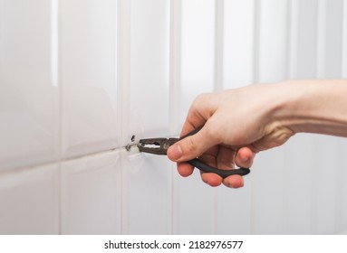 The hands of a young caucasian guy are pulling out a stuck and old dowel from a hole in a tiled wall