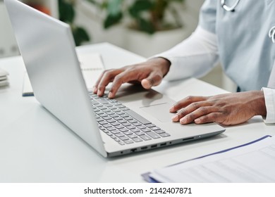 Hands of young contemporary African American male online doctor over laptop keyboard answering questions of patients in clinics