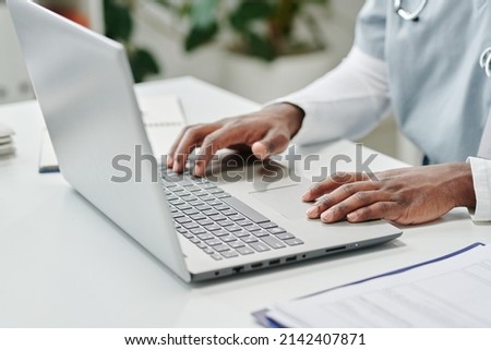 Hands of young contemporary African American male online doctor over laptop keyboard answering questions of patients in clinics