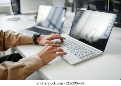 Hands of young contemporary program developer typing on laptop keyboard while sitting by desk in office or bureau - Shutterstock ID 2120006489