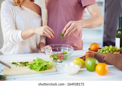 Hands of young couple adding cut parsley into bowl with fresh vegetarian salad - Powered by Shutterstock