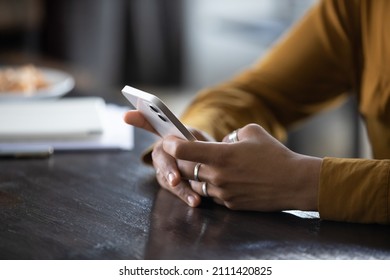 Hands of young dark skinned woman with finger rings using online app on mobile phone, making call, browsing Internet, chatting on social media, holding cellphone, texting, typing message. Close up