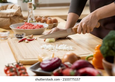 Manos de una joven hembra cortando cebolla fresca en tablas de madera mientras prepara pasta italiana con verduras y carne picada
