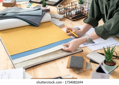 Hands of young female creative designer of interior choosing wallpapers and furniture textile while working over new order of client - Shutterstock ID 1734082694
