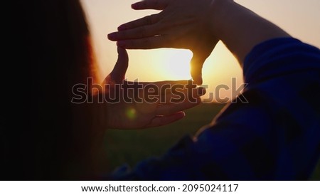 Hands of a young female director cameraman making a frame gesture at sunset. The concept of seeing the world as different. Business planning. The girl shows her fingers a frame symbol in the sun