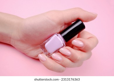The hands of a young girl hold a bottle of pink gel nail polish on a pink background.The concept of hand and nail care, manicure, beauty salon, nail extension - Powered by Shutterstock