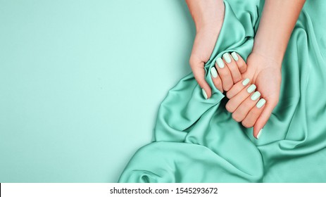 Hands Of A Young Girl On A Mint Silk Cloth, Manicure On A Trendy Background , Green Polish