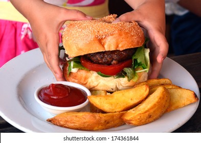 Hands Of A Young Girl Ready To Eat A Big Hamburger. Concept Photo Of Child Obesity, Unhealthy Eating, Unhealthy Food. Real People. Copy Space