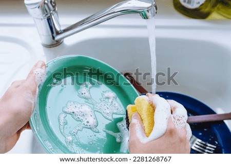 hands young girl wash plate with kitchen sponge with dish detergent, in kitchen sink, under stream of water. concept of washing dishes, natural detergents. Concept kitchen, morning, woman, dishwasher