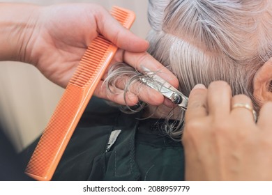 Hands of a young hairdresser cutting the hair of an old lady. Lifestyle.
