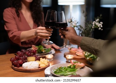 Hands of young interracial dates clinking with glasses of red wine over dinner table served with healthy food and snacks - Powered by Shutterstock