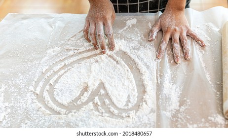 Hands of a young lady working with bakery flour and drawing heart shape on the table. Girl enjoys preparing materials for making bakery products - Powered by Shutterstock