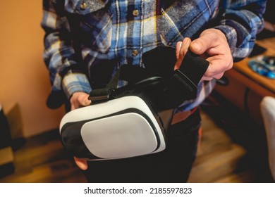 Hands Of Young Latino Man With Plaid Shirt Holding A Virtual Reality Helmet (VR Glasses) In Orange Bedroom On Home