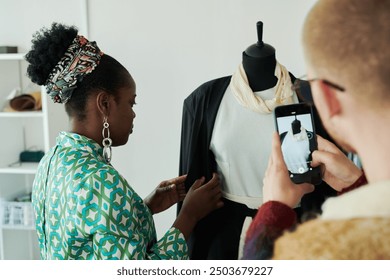 Hands of young male fashion designer with smartphone taking picture of female colleague creating new dress or costume on mannequin - Powered by Shutterstock