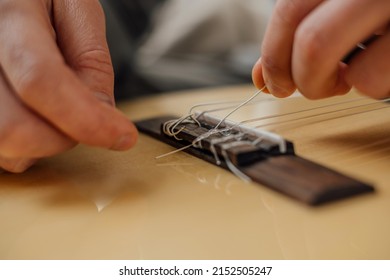 Hands of a young man changing the string on an acoustic guitar.