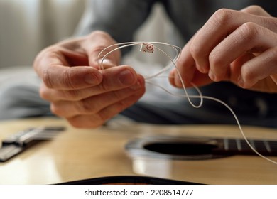 Hands of a young man changing the string on an acoustic guitar. Musical instrument.